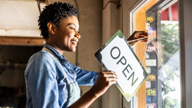 Business owner hanging an “OPEN” sign on a shop door.