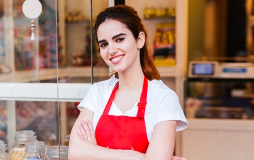 Smiling woman in a red apron outside of a local food store