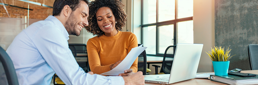 A man and woman sitting in front of a laptop looking at a business document