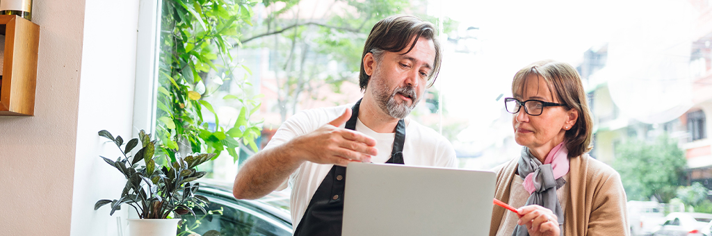 A man and woman talking while looking at a laptop screen.