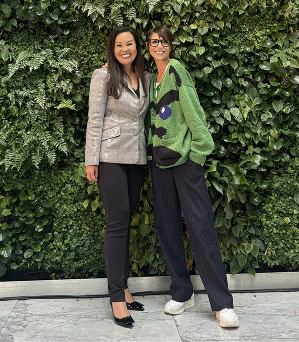 Two women posing in front of a greenery backdrop