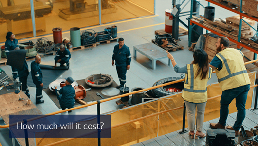 Two people discuss the goings-on below them on a factory floor. Text reads how much will it cost?