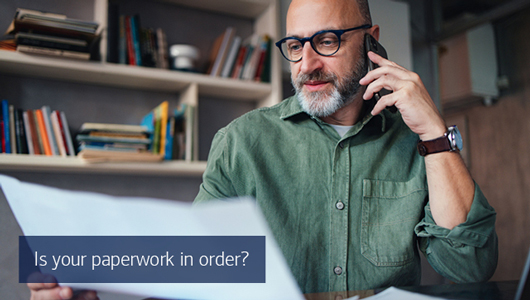 A man on the telephone studies a piece of paper. Text reads is your paperwork in order?