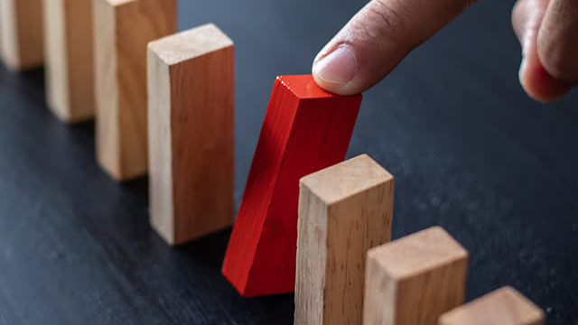 Wooden blocks with a hand stopping a red block.